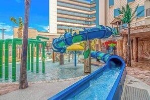 A water park with slides and a pool area, surrounded by palm trees and a building with horizontal windows. - Updated 3BR w/ Views & Waterpark (Myrtle Beach)