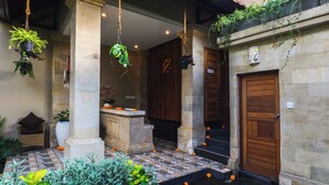 A courtyard with a stone bench, hanging plants, and a wooden door. - Elemara  (Ubud)