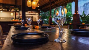A restaurant setting with a wooden table, wine glasses, and a black plate. - Elemara  (Ubud)