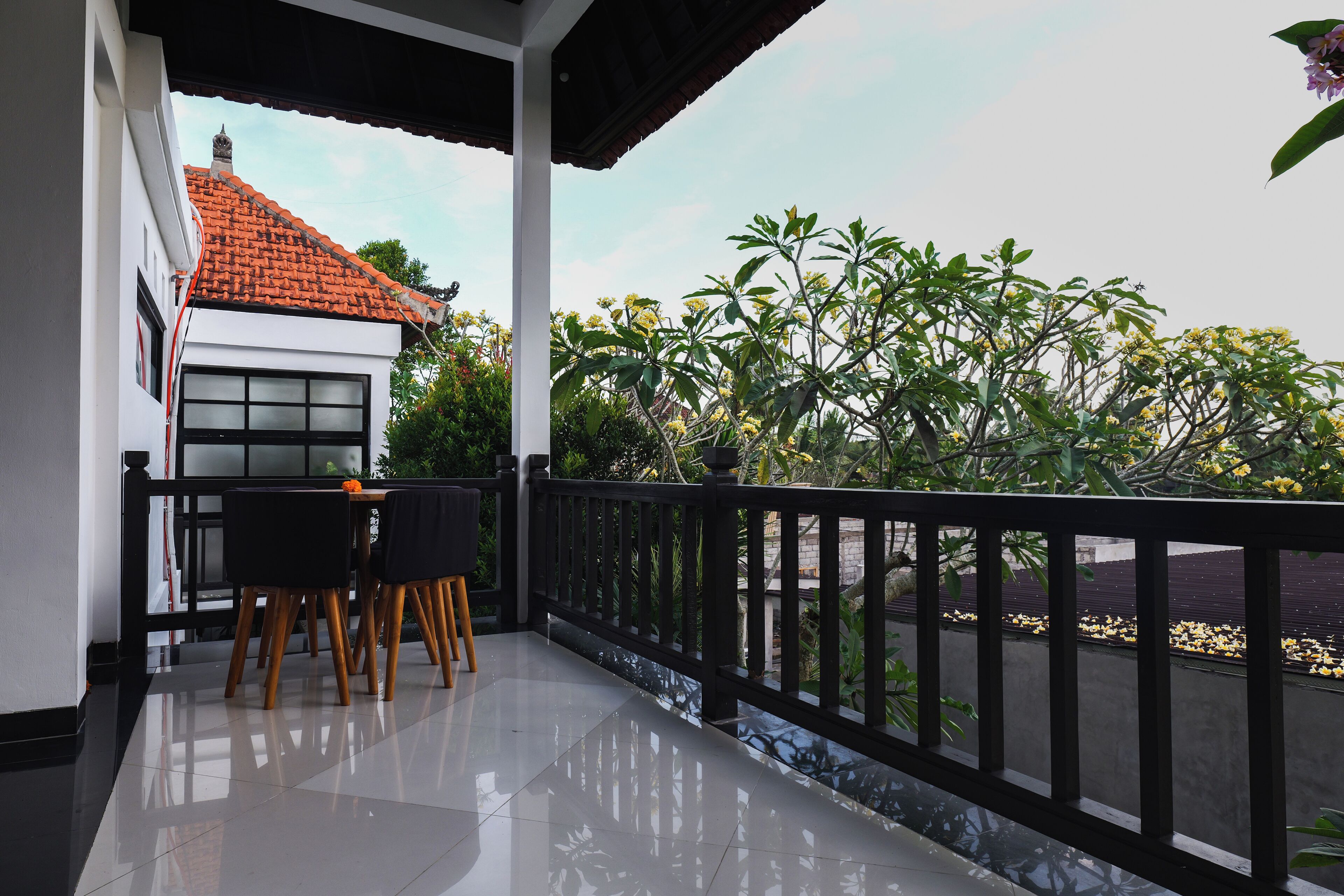 A balcony with a table and chairs, a tiled floor, and a view of a house and greenery.