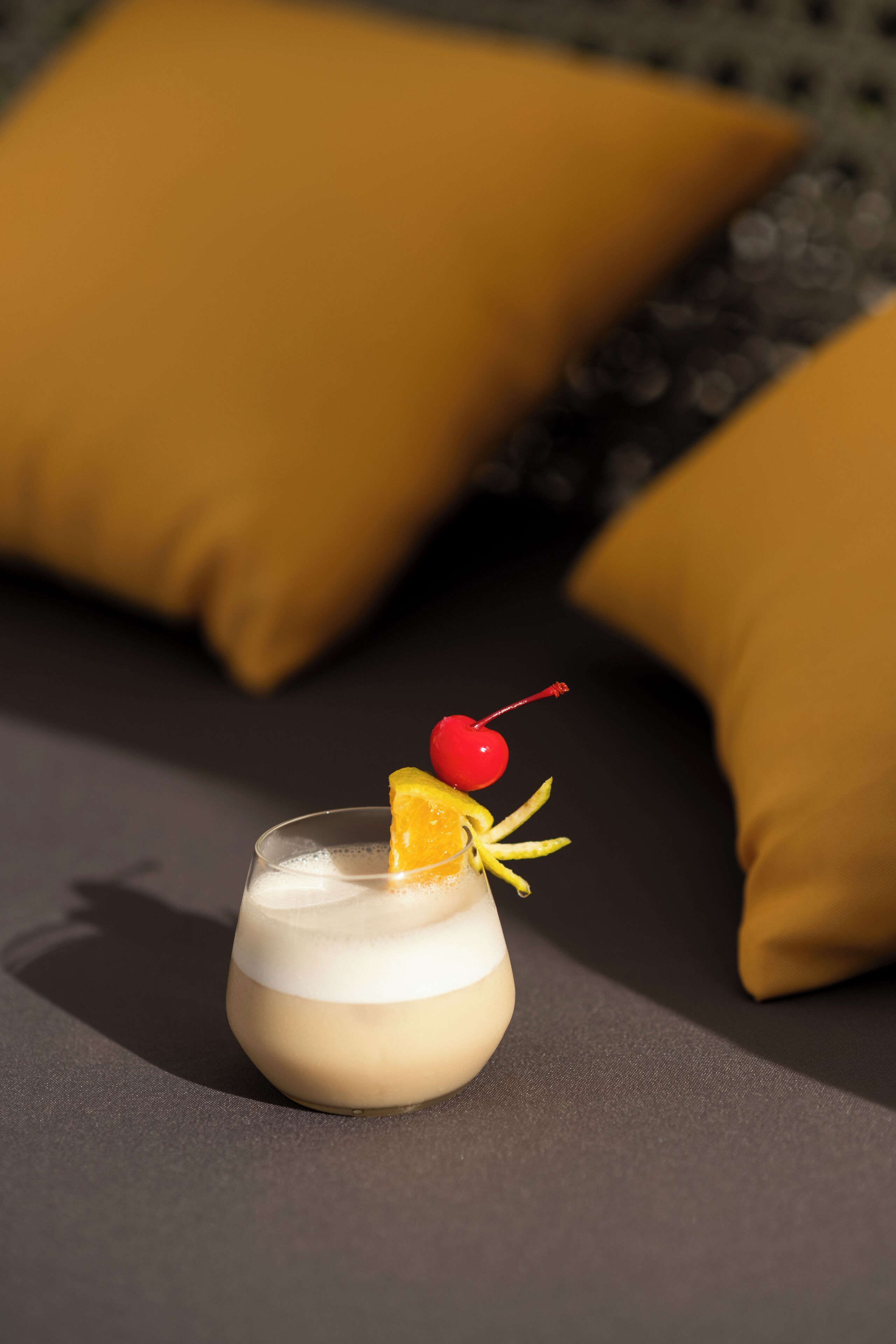 A glass of a creamy beverage with a cherry and orange slice garnish on a dark surface.