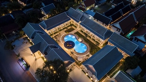 Vista aérea de un hotel con piscina central, varias habitaciones de huéspedes y un área exterior bien iluminada.