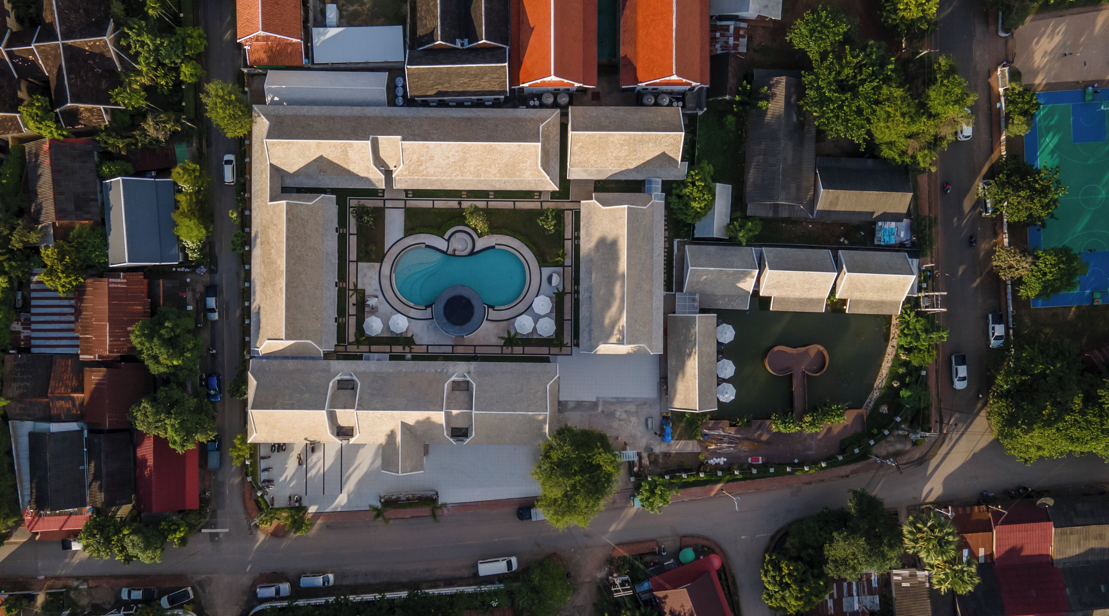 An aerial view of a hotel with a central swimming pool, multiple guest rooms, and a parking area.