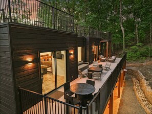 Une cabane moderne en bois dotée d’un balcon, aménagée avec des meubles de jardin et une table.