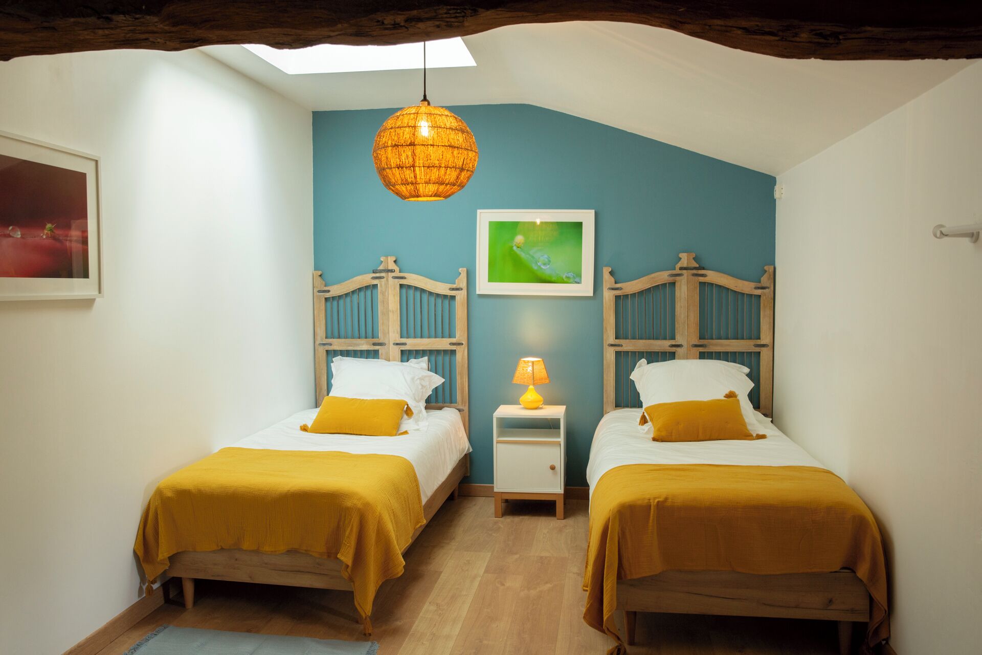 Un dormitorio con dos camas de madera, una lámpara colgante, una mesita de noche pequeña con lámpara y un cuadro enmarcado en la pared.