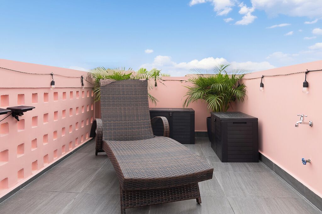A rooftop terrace with a wicker lounge chair, a small table, potted plants, and a water feature.