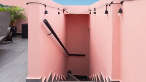 Een wenteltrap met roze wanden, een zwarre leuning en een lamp erboven.