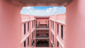 Een roze meerlaagsgebouw met balkons en een open ruimte in het midden.