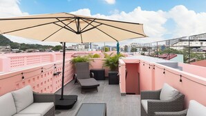 Een terras op het dak met buitenmeubilair, een grote parasol en uitzicht op de stad.