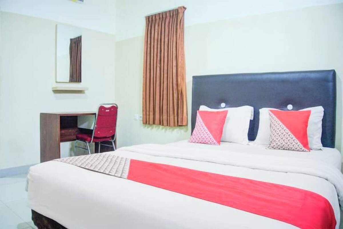 Habitación de hotel con cama, escritorio, silla, ventana con cortinas y espejo en la pared.