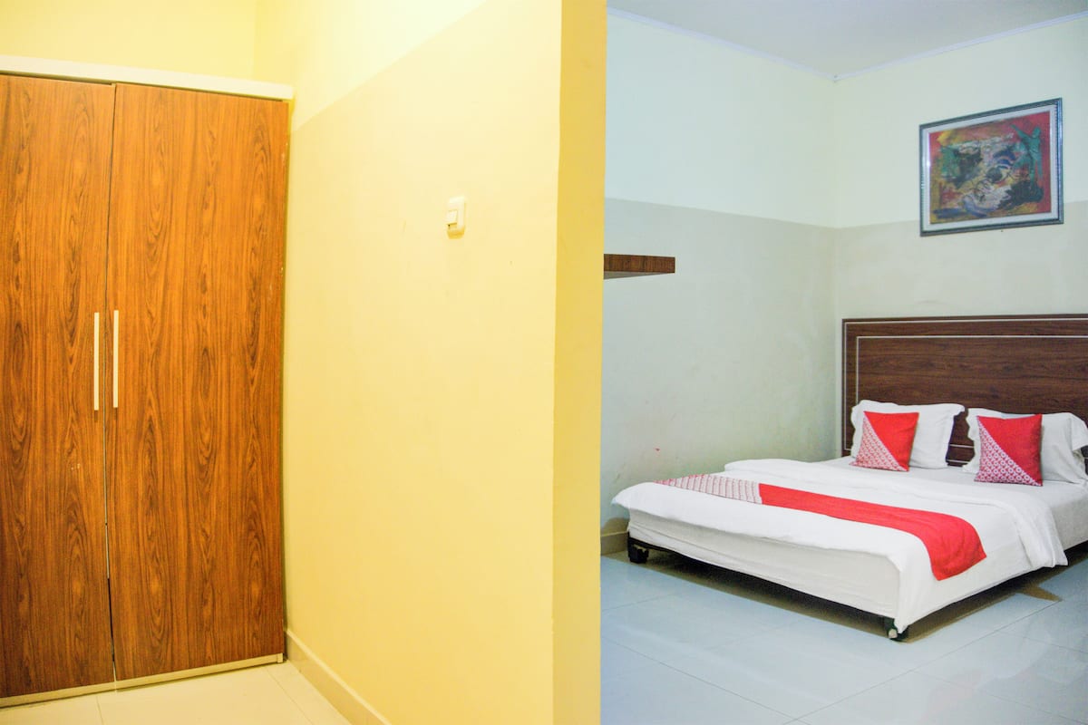 Un dormitorio con un armario de madera, una cama con ropa de cama roja y blanca, y un cuadro en la pared.