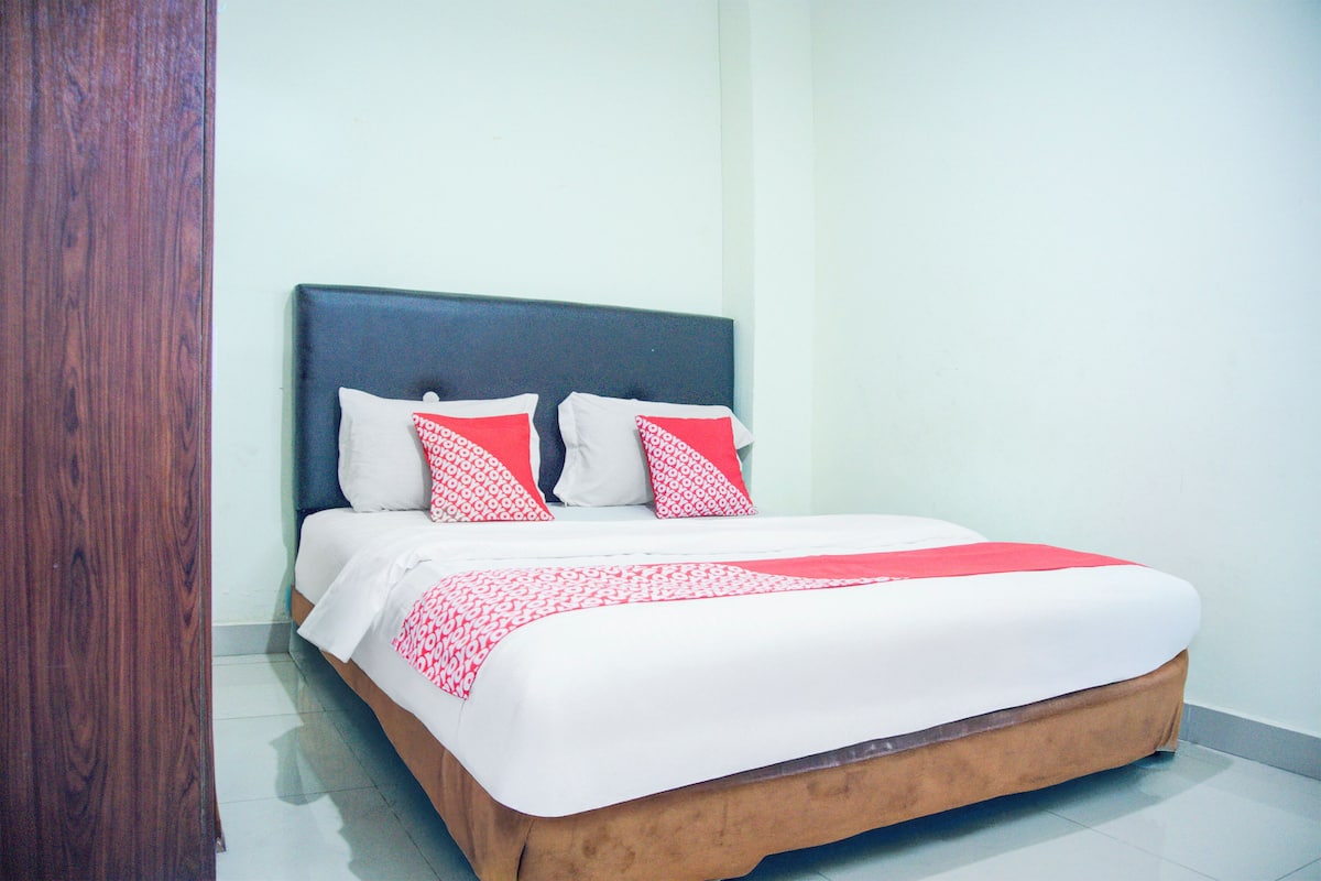 Una cama bien hecha con ropa de cama blanca y roja, un cabecero oscuro y suelo de madera.