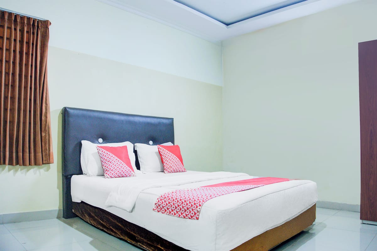Una cama bien tendida con cabecera oscura, ropa de cama blanca y detalles en rosa.
