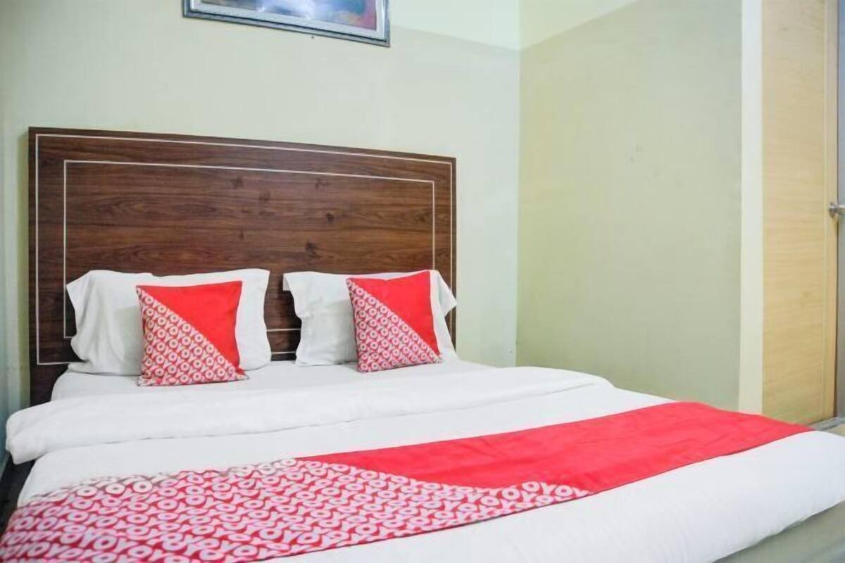Una cama con cabecera de madera, ropa de cama blanca y roja, y una colcha roja estampada.