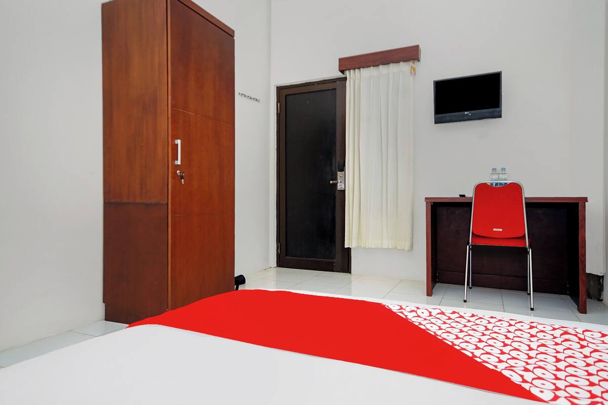 A room with a bed, a desk, a chair, a wardrobe, a television, and a door with curtains.