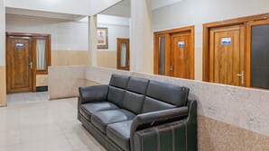 A hotel lobby with a black leather sofa, wooden doors, and a tiled floor. - Hotel O Ilir Barar I Near Rumah Sakit Islam Siti Khadijah Formerly Maleo Hotel (Palembang)