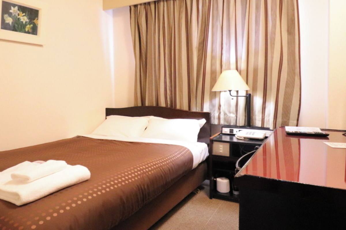 A hotel room with a bed, a desk, a lamp, and a curtain.