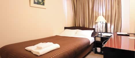 A hotel room with a bed, a desk, a lamp, and a curtain.