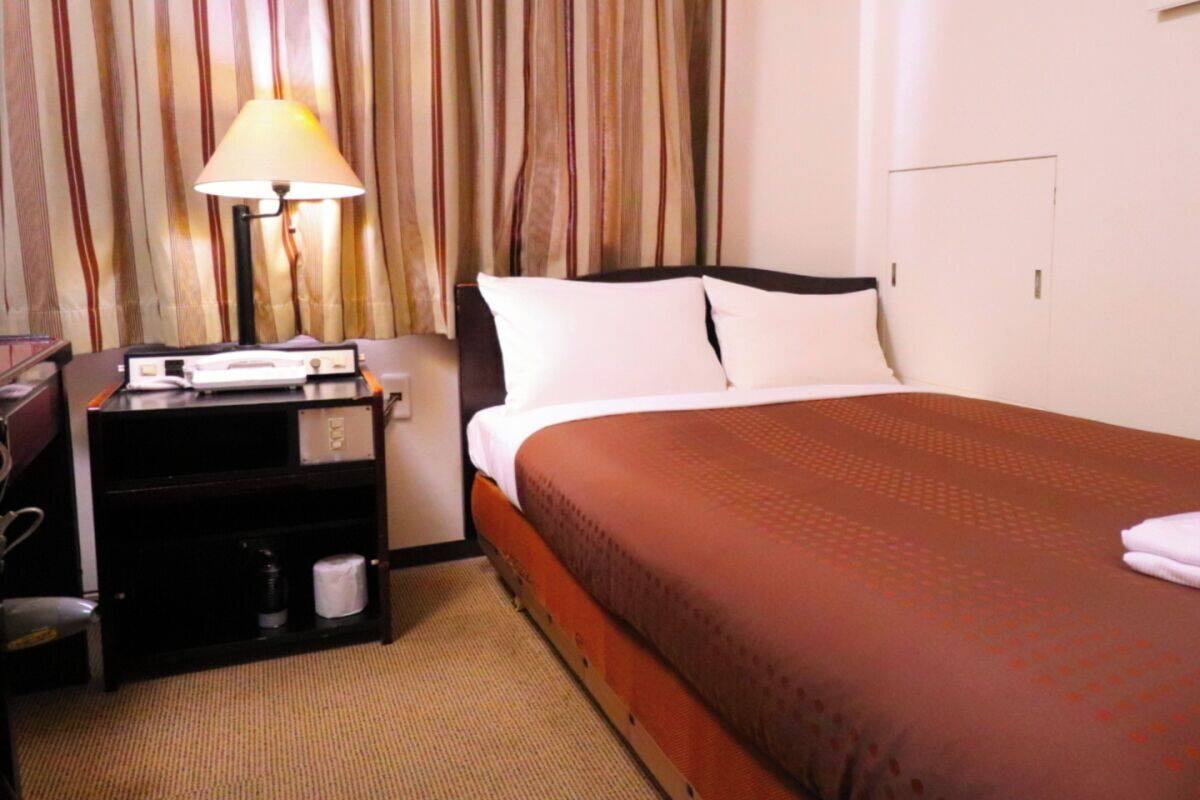 A hotel room with a bed, a nightstand, a lamp, and a curtain.