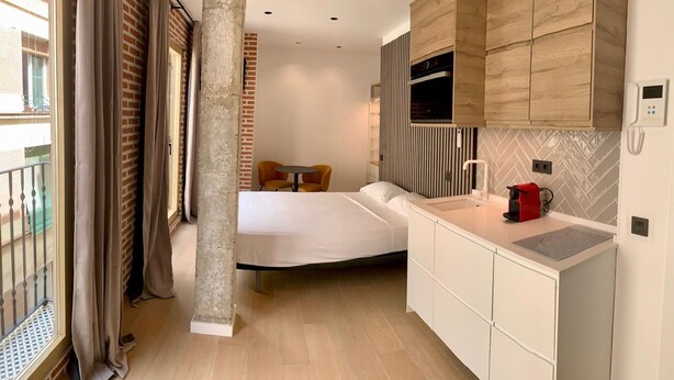 A compact hotel room with a kitchenette, a bed, and a balcony with curtains.