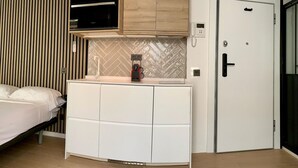 A modern bedroom with a bed, a white wardrobe, a built-in oven, and a door with a phone and a lock.