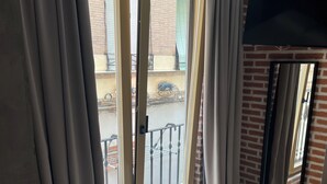 A hotel room with a bed, a TV mounted on the wall, and a balcony with a view of the street and parked bicycles.