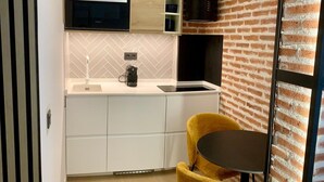 Une cuisine moderne avec des meubles blancs, un four encastré et une hotte noire. On y trouve une chaise jaune et une petite table ronde dans l’espace repas.