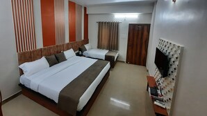 Een hotelkamer met een groot bed, een kleiner bed, een plafondventilator, een aan de muur bevestigde televisie, en een deur met een bordje.