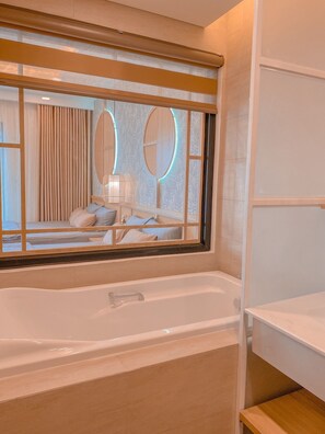 Un baño moderno con una bañera grande, un tocador con espejo y un ventanal con persianas.