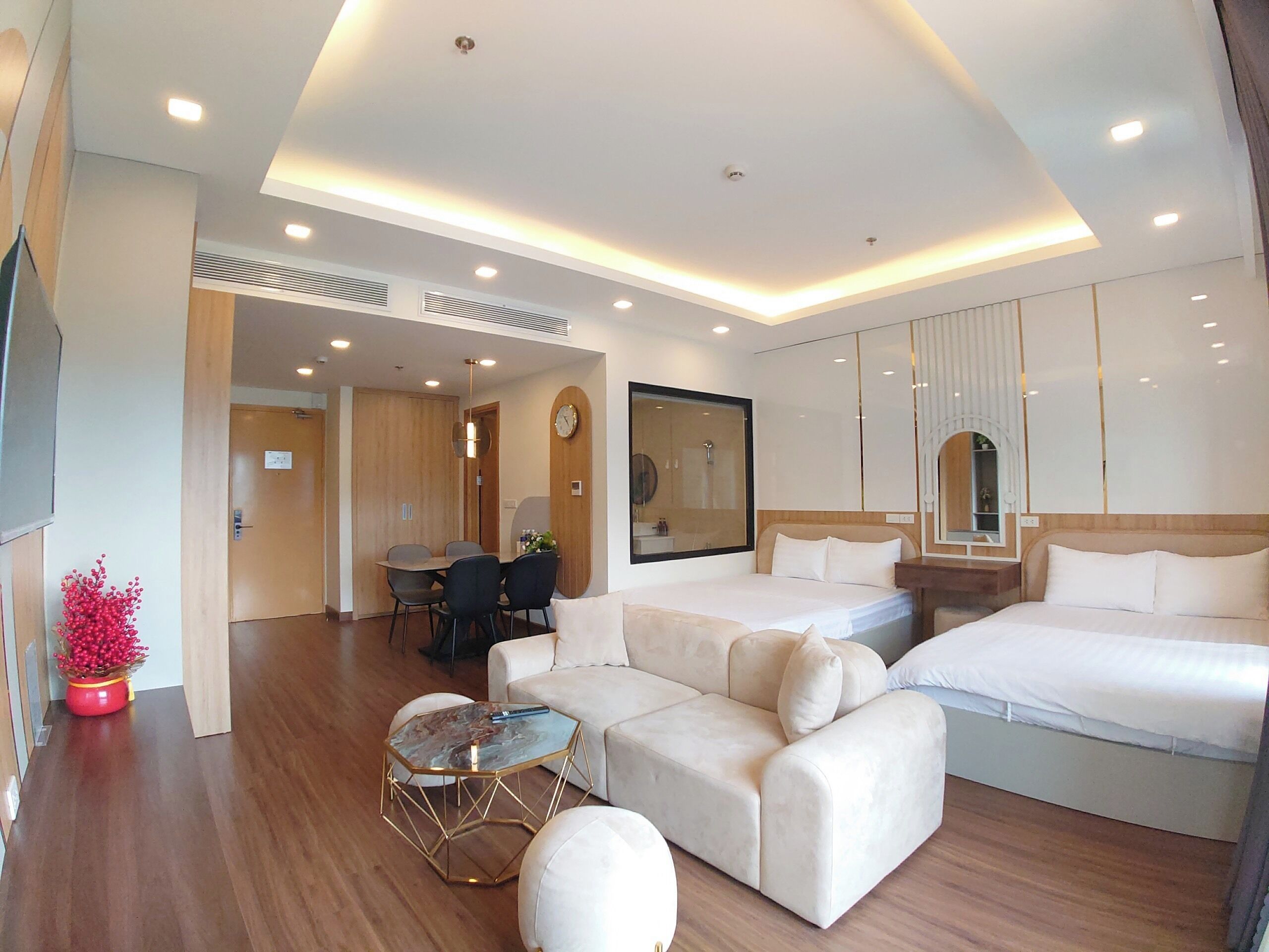 Habitació d'hotel moderna amb sofà, dos llits, zona de menjador i bany amb un mirall gran.