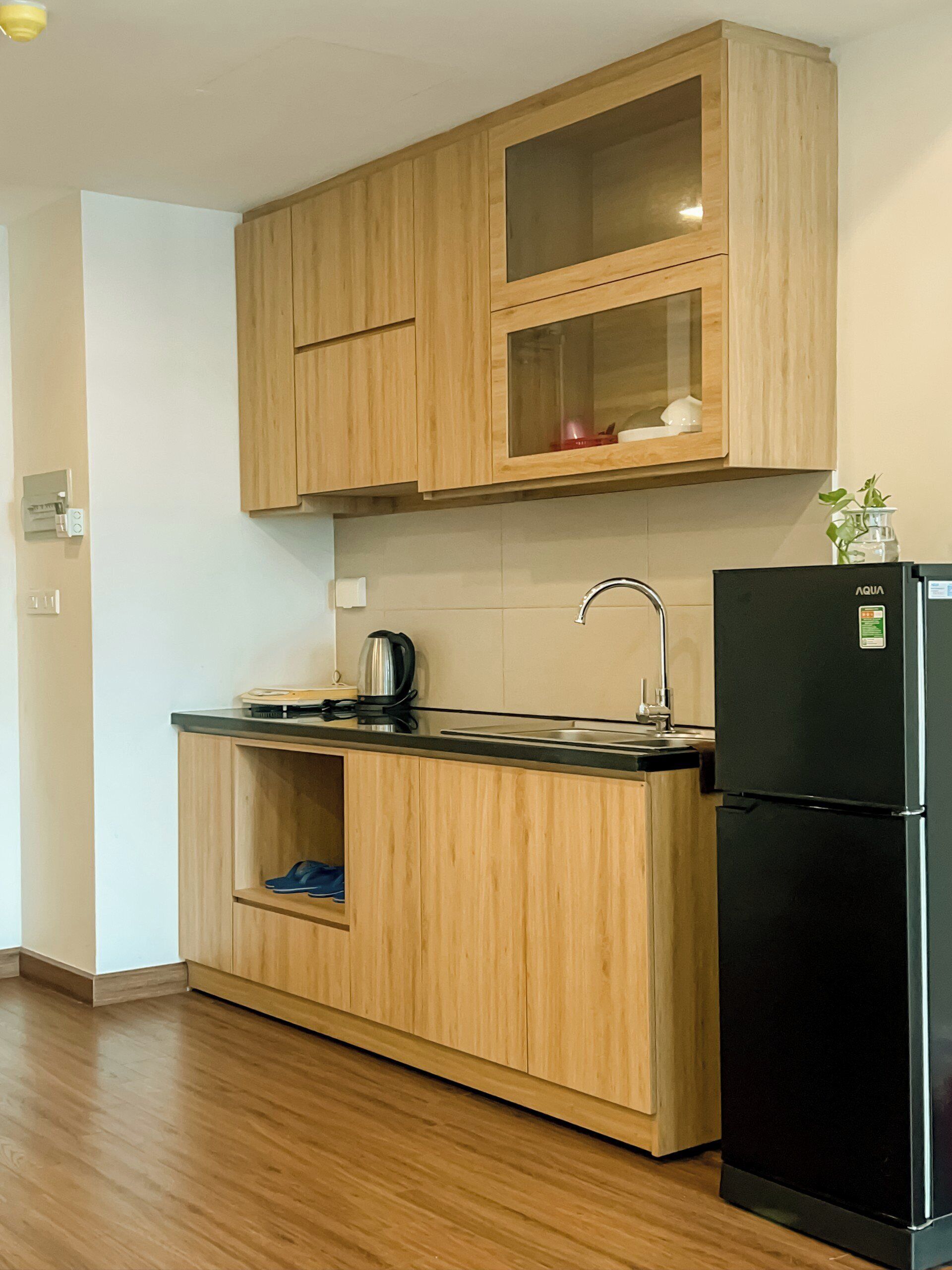 Una cocina con armarios de madera, un refrigerador negro y un lavamanos de acero inoxidable.