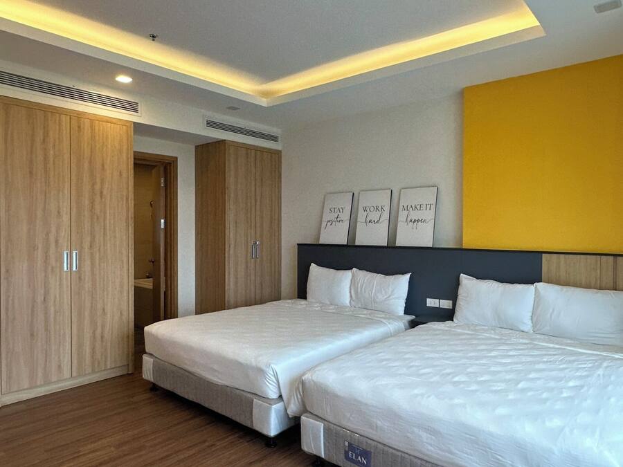 Quarto de hotel moderno com duas camas, um guarda-roupa de madeira e arte motivacional na parede.