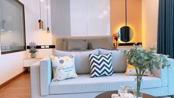 A modern living room with a light grey sofa, two patterned throw pillows, a round mirror, and a small table with decorative items.