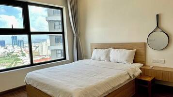 Una habitación de hotel moderna con una cama grande, piso de madera, vistas a la ciudad y una mesita de noche sencilla.