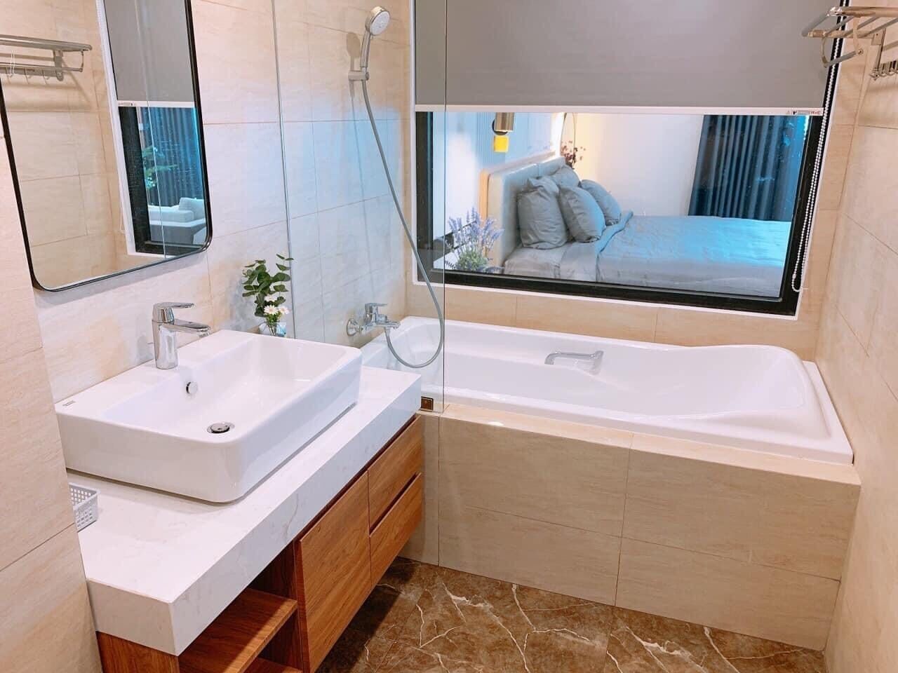 Un baño moderno con una bañera grande, un lavamanos doble y una ventana con vista a un dormitorio.