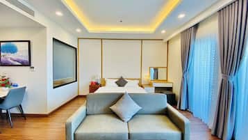 A hotel room with a sofa, a bed, a desk, and a large window with curtains.