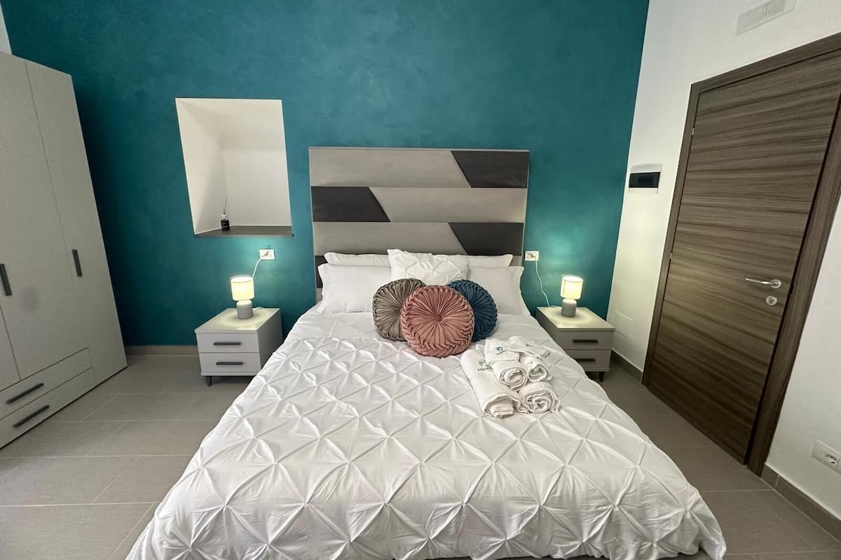 A neatly made bed with a geometric patterned duvet, two bedside lamps, and a teal accent wall.