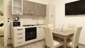 Een moderne keuken met witte kastjes, een magnetron, kookplaat en een eethoek met een tafel en stoelen.