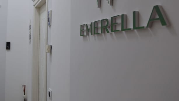 Een gang met een witte muur waarop een abstract ontwerp in groen en wit is afgebeeld en de tekst 'EMERELLA' in groene letters staat.