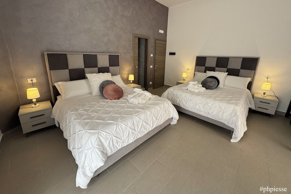 A hotel room with two beds, each with a headboard, bedside tables, and lamps.
