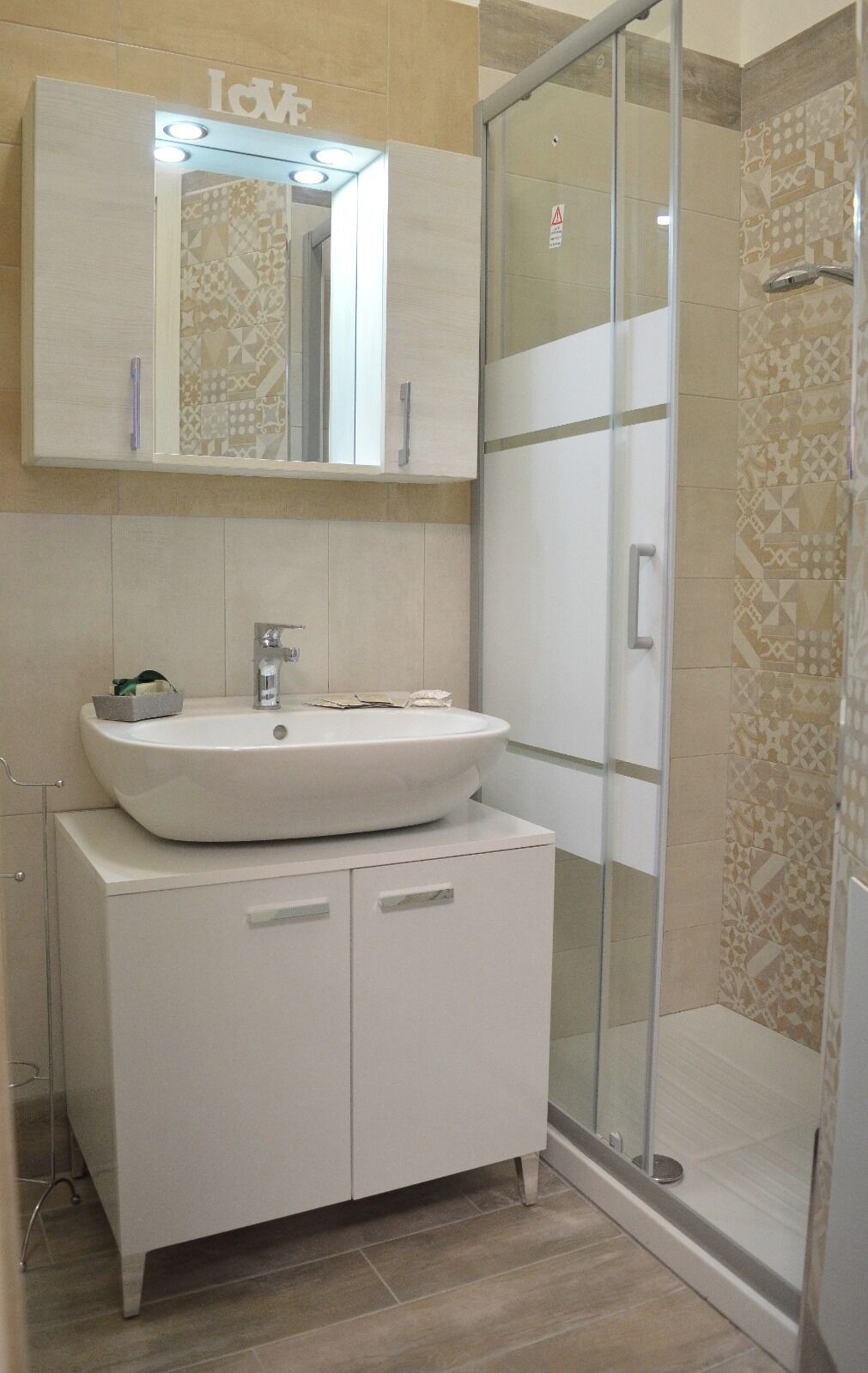 A bathroom with a white sink, a mirror above it, and a shower area with patterned tiles.