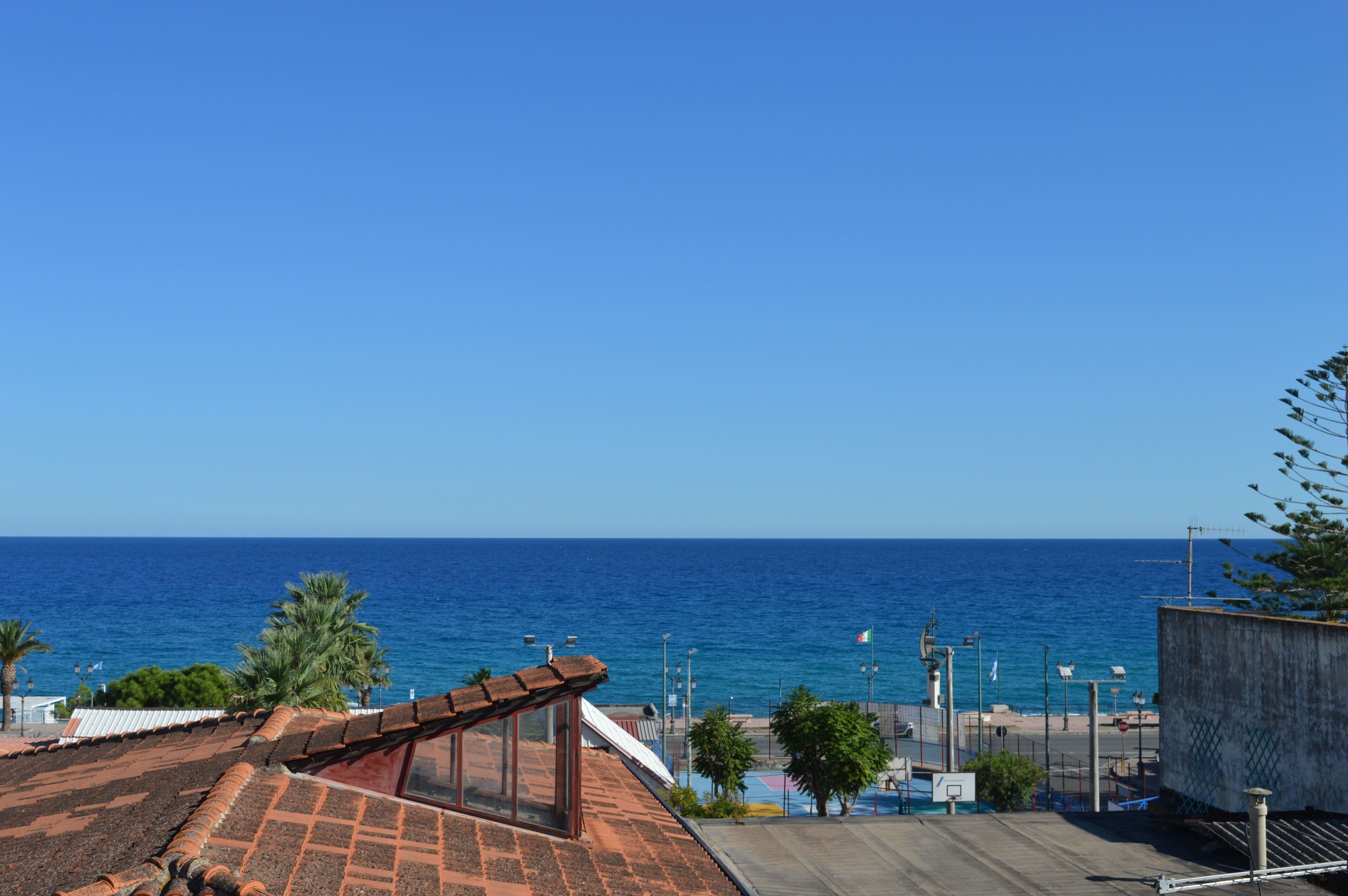 A coastal view with a clear sky, a beach, and a building with a tiled roof.