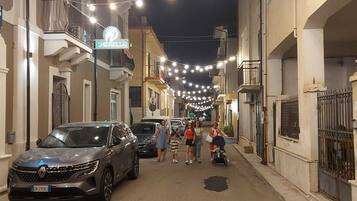 Una strada fiancheggiata da edifici, con luci decorative appese e auto parcheggiate.