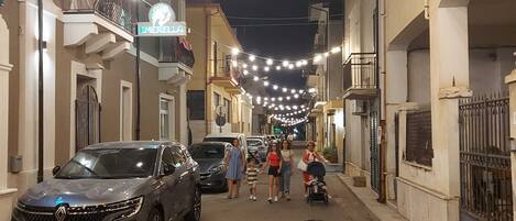 A street lined with buildings, string lights overhead, and parked cars.