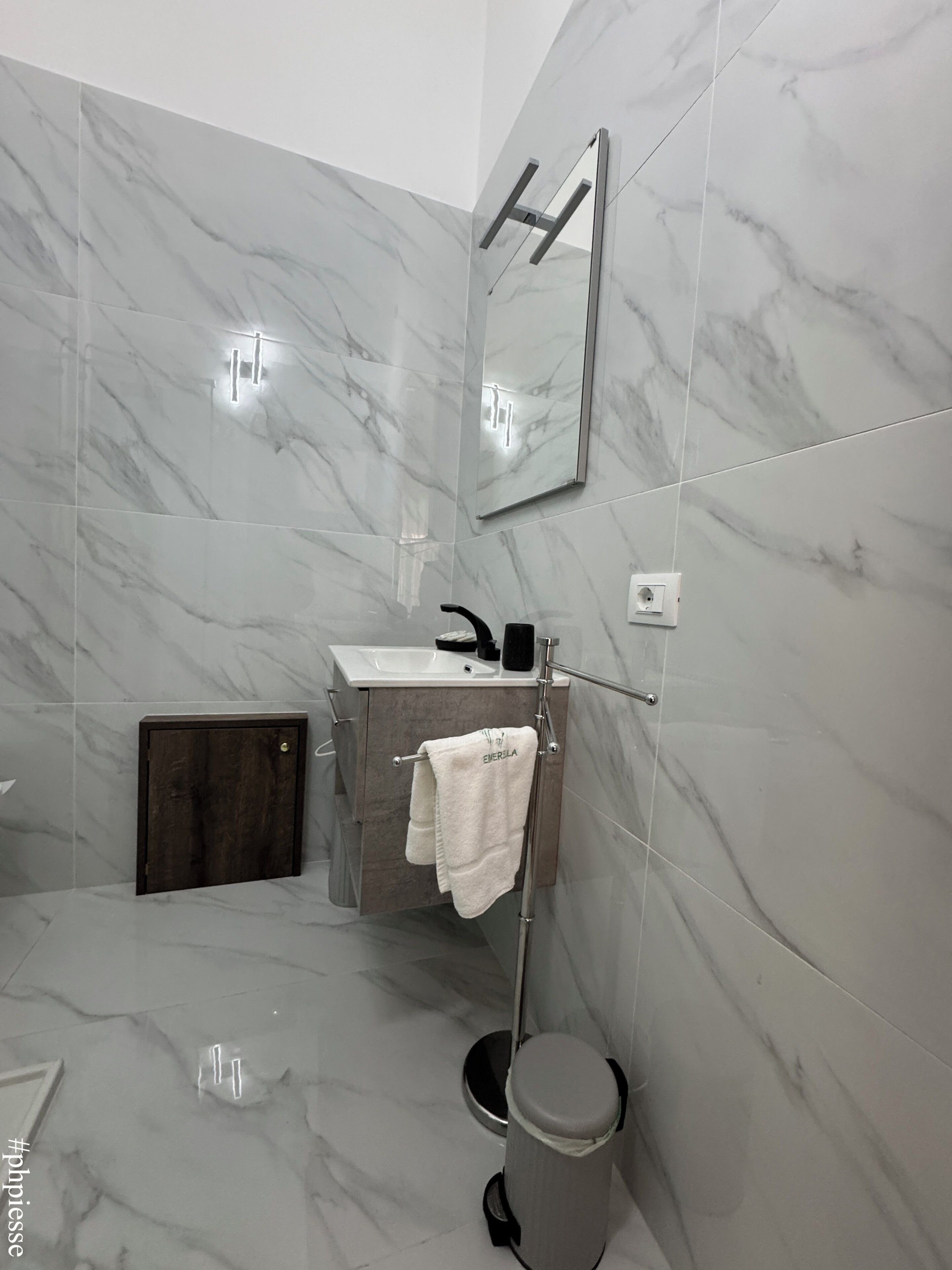 Un baño moderno con paredes de mármol, un lavamanos, un espejo y un perchero para toallas.