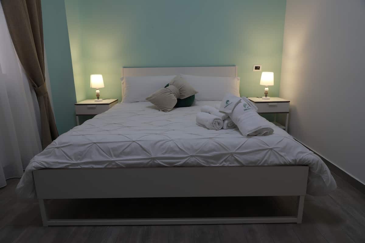 A hotel room with a bed, two bedside tables with lamps, a headboard, and a window with curtains.