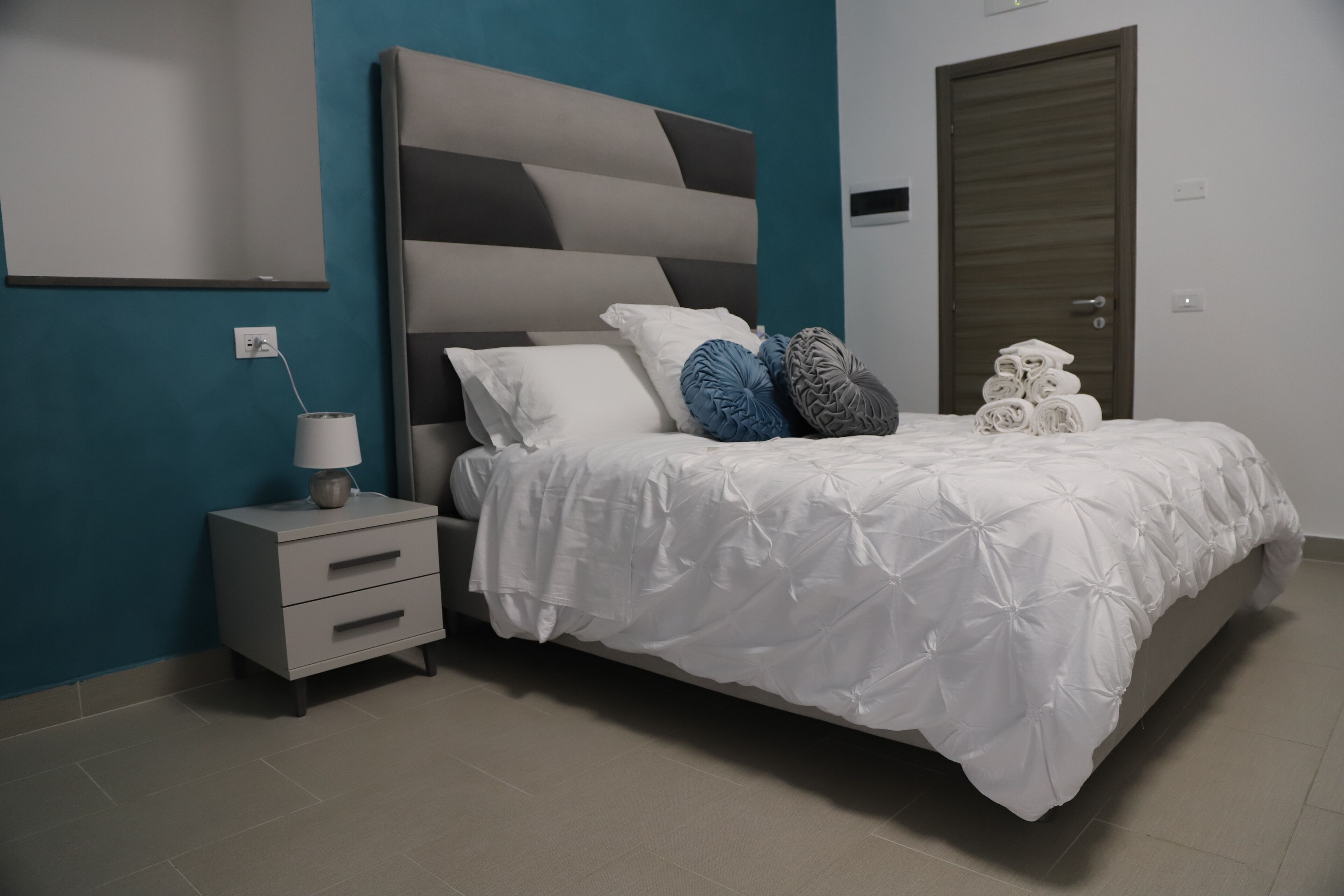 A bedroom with a bed, a nightstand, a lamp, and a door.