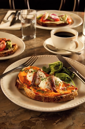A dining table with plates of food, a cup of coffee, and cutlery. - Hotel Indigo Auckland by IHG (Auckland)