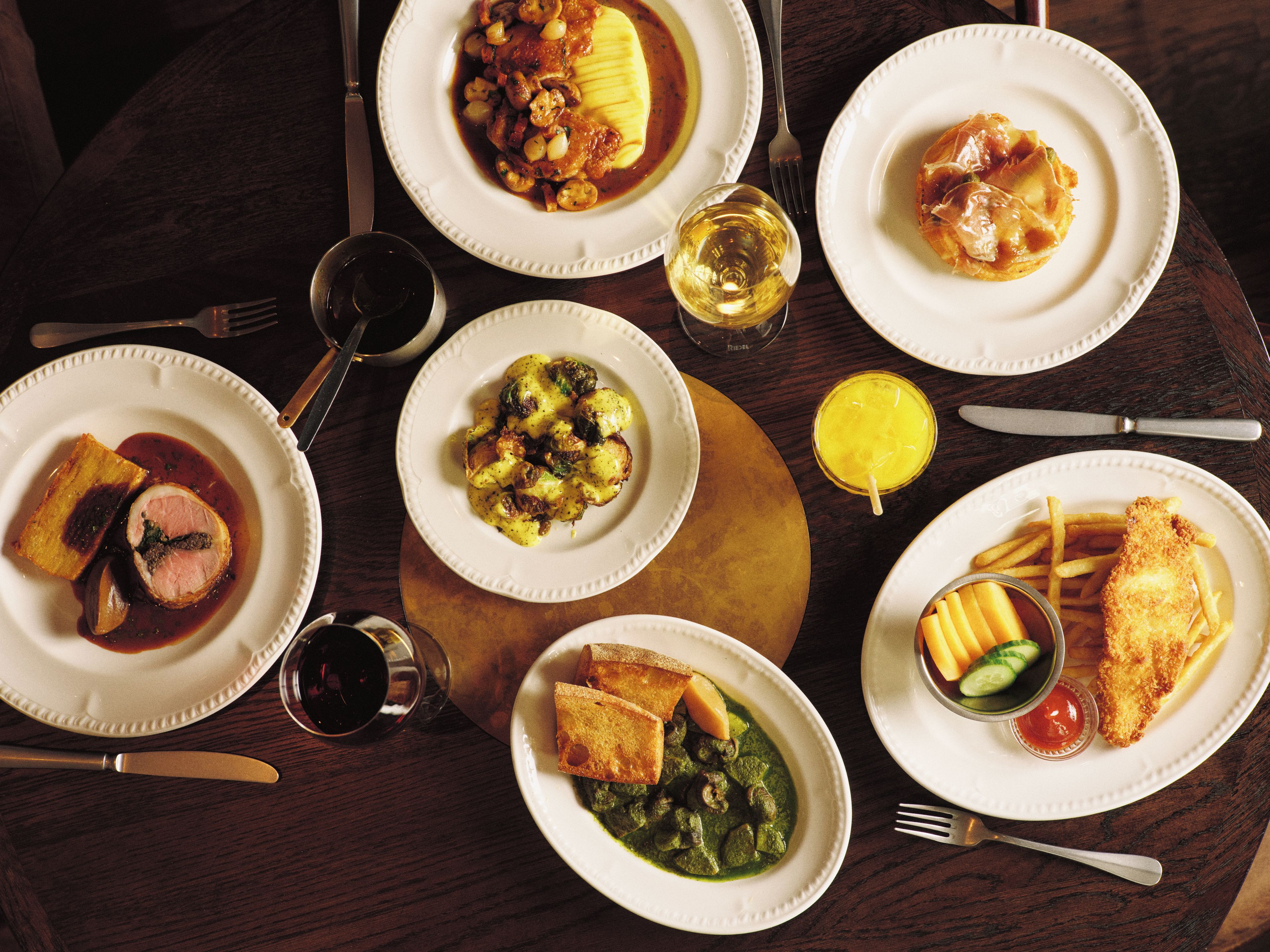 A table with various dishes, including a steak, a green sauce dish, and a plate with fries and a breaded item.