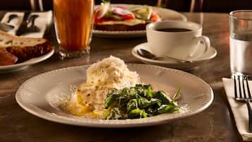 Un plato de comida con un guiso cremoso y vegetales verdes, una taza de café y un vaso de agua sobre una mesa.